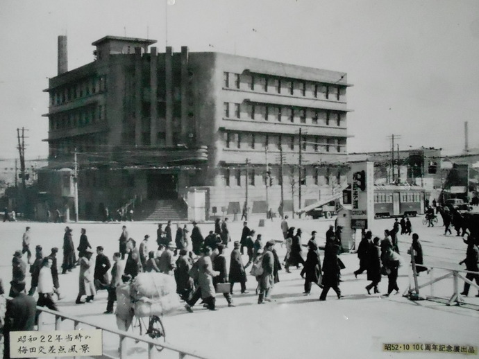 奥に三代目曽根崎警察署庁舎があり、手前の梅田交差点を人々が行き交っている白黒写真