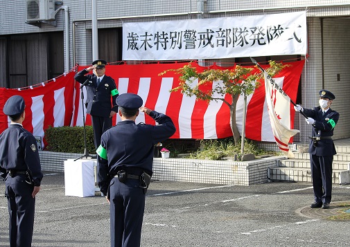歳末特別警戒部隊発隊式と書かれた横断幕と紅白の横断幕の前で、壇上に上がり敬礼する警察官と向かい合って敬礼する警察官と背筋を伸ばし気をつけをしている警察官の写真