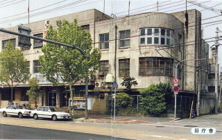 街路樹が並んだ街角に、角が丸みを帯びた3階建ての大きな旧庁舎が建っている写真