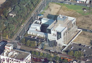 林や広場が周りにある街角に、白い建物が建っている様子を上空から撮った写真