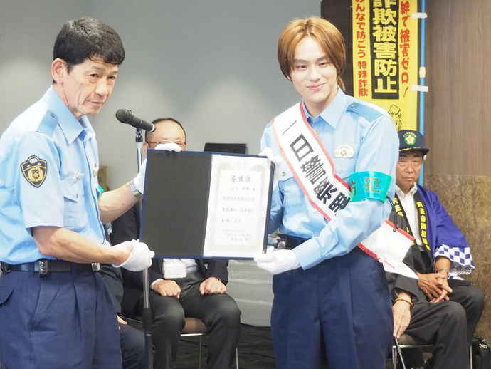 警察官の方と「一日警察署長」のたすきを付けた山下幸輝さんが委嘱状を2人で持っている様子の写真