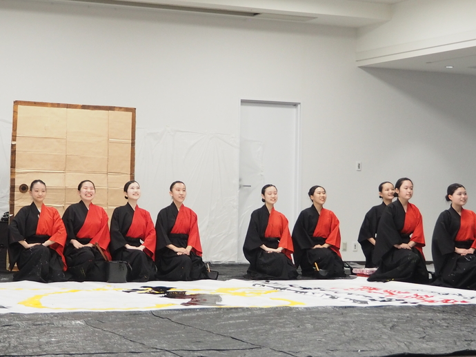 赤と黒の袴を着て正座をしている上宮高校書道パフォーマンス部の皆さんの写真
