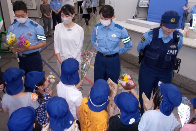 制服を着た男性・女性警察官と、受付の女性に小さな花束を渡している青い帽子を被った子ども達の写真