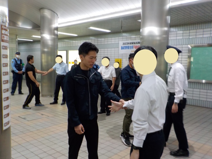 駅のホームにて、手を広げて前に出している人と、相手の手首を握っている人が二人一組になって訓練をしている様子の写真