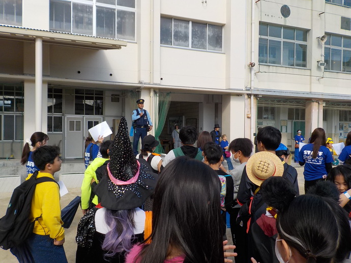 小学校の校庭で防犯や交通安全の呼びかけをしている警察官と話を聞いている子供たちの写真