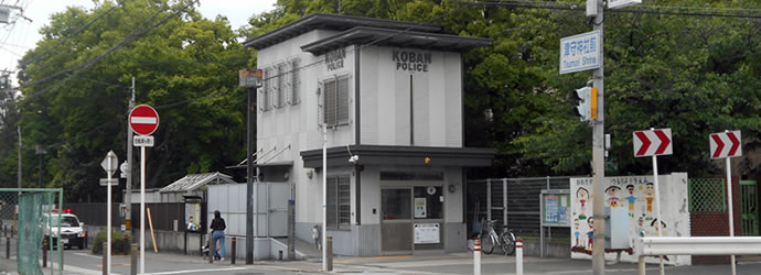 「津守神社前」交差点近くに建っている木々に囲まれ2階建てで壁が灰色の中津守交番の外観写真