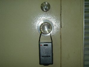 ドアノブにぶら下げられている黒色で携帯電話のような形をしている防犯ドアブザーの写真