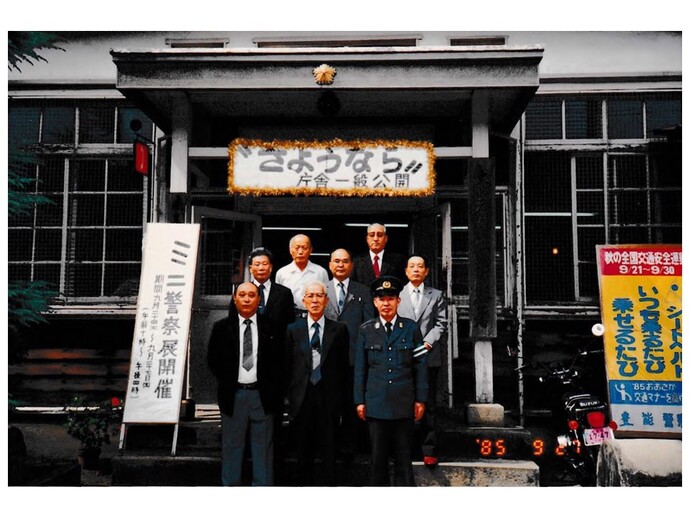 「さようなら 庁舎一般公開」と書かれた看板が旧庁舎入口上部に掲げられ、警察官の方、関係者の方8名が3列に並び、入り口前で記念撮影を行っている写真
