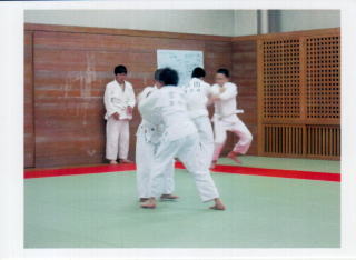 道場の壁側で見学をしている子どもや互いの柔道着の襟元を掴み、稽古をしている2組の子どもたちの写真