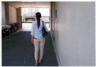 女性が車道と反対側の右肩に黒いカバンを掛け、右側の壁に沿って歩いている写真