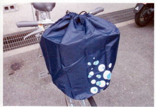 自転車の前かごに取り付けられている紺色地にシャボン玉模様のついた巾着式ひったくり防止カバーの開口部がしっかりと絞められた状態の写真