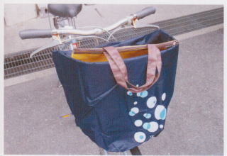 自転車の前かごに取り付けられている紺色地にシャボン玉模様のついたひったくり防止カバーが開いており、上からバッグが見えている写真