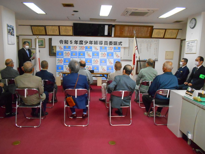 前方左側に立ち文書を読み上げている警察署員と椅子に座って話を聞いている委嘱式の参加者と2名の警察署員の写真