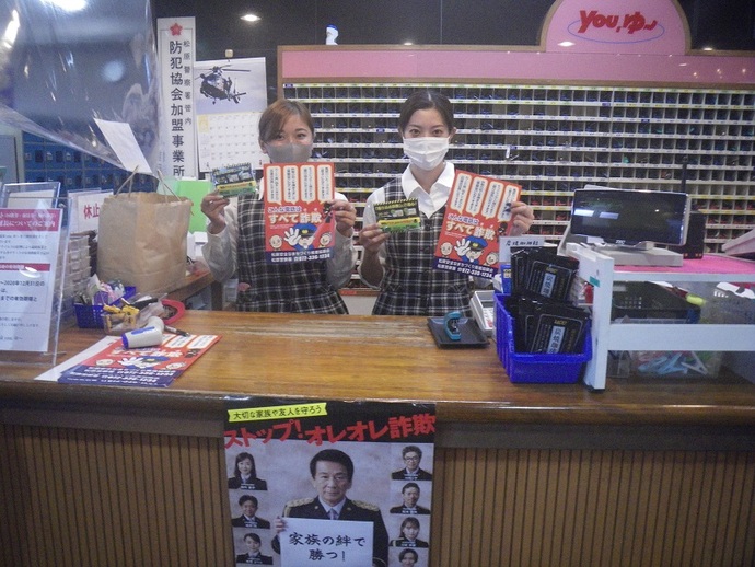 松原天然温泉you、ゆ～フロントの女性従業員2人が、詐欺予防啓発チラシを両手に持っている写真